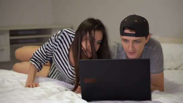Молодая пара парень и девушка лежат перед ноутбуком и говорят — стоковое видео