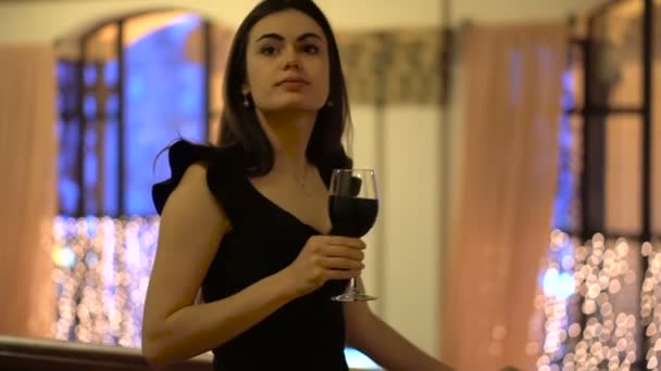 Девушка смотрит вокруг и пьет красное вино — стоковое видео