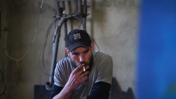 Muž v čepici a s plnovousem kouří a vypadá — Stock video