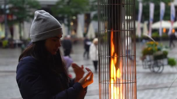 Девушка холодная и согревает руки с помощью уличных газовых обогревателей — стоковое видео
