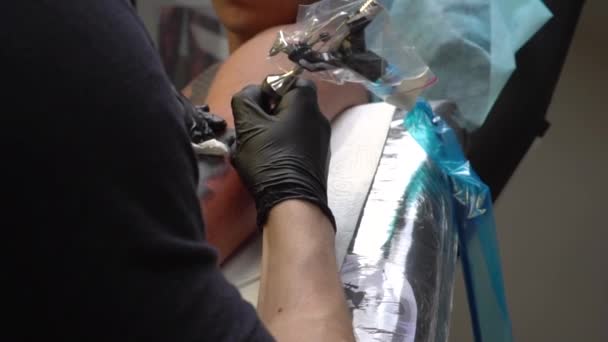 Tatuaje salón chico con auriculares Bluetooth hace un tatuaje a otro chico — Vídeo de stock