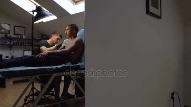 Tatuażysta praca z klientem, leżąc na kanapie podczas tworzenia tatuaż — Wideo stockowe