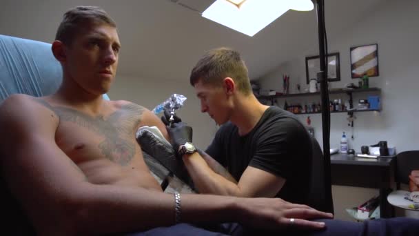 Два парня серьезно посмотрите один из них делает татуировку — стоковое видео