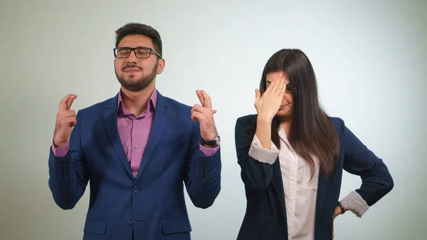 Business partner crossed their fingers the girl funny criticizes her colleague who has closed eyes happily raised his head in prayer Royalty Free Stock Photos