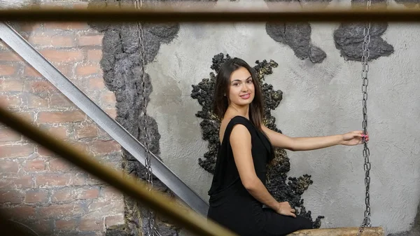 Bir buçuk zincirlerle ahşap bir salıncak oturan siyah tulum gülümsüyor kız esmer açmak