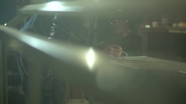 Механічний дорослий чоловік в чорній куртці і шапці малює пензлем на витяжці автомобіля в гаражі — стокове відео
