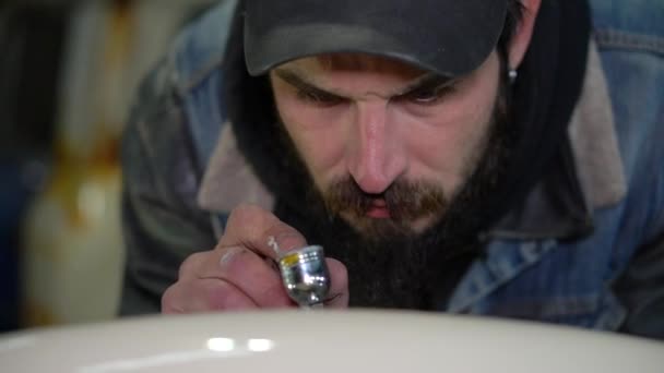 Retrato de un hombre barbudo adulto en una gorra con tatuajes dibujo con aerógrafo en taller — Vídeo de stock