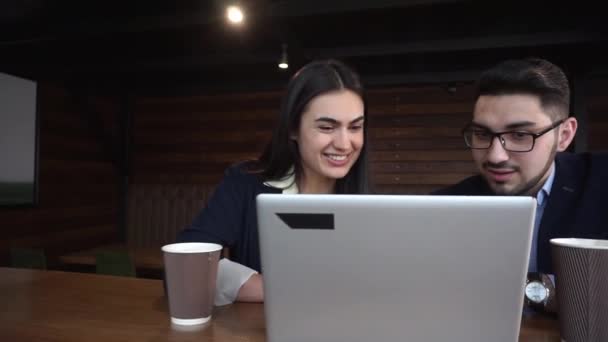 Junger Mann und fröhliche Frau schauen auf einen Laptop, der im Café sitzt — Stockvideo