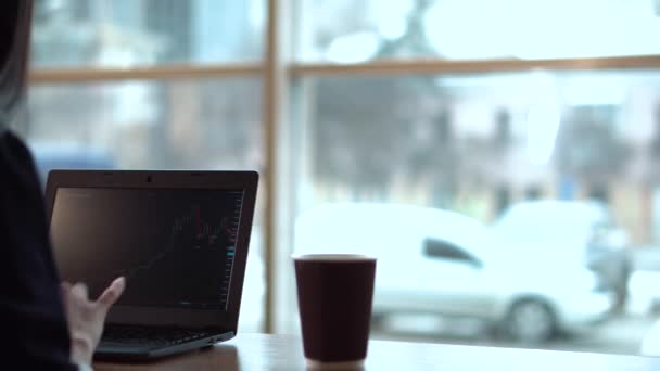 Brünettes Mädchen verfolgt Börsencharts am Laptop und trinkt oft Kaffee — Stockvideo