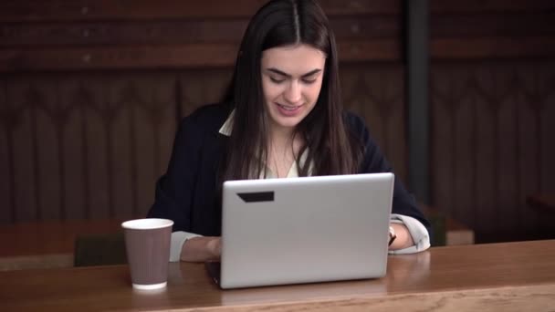 Lächelndes brünettes Mädchen im Café tippt auf Laptop und trinkt Kaffee — Stockvideo