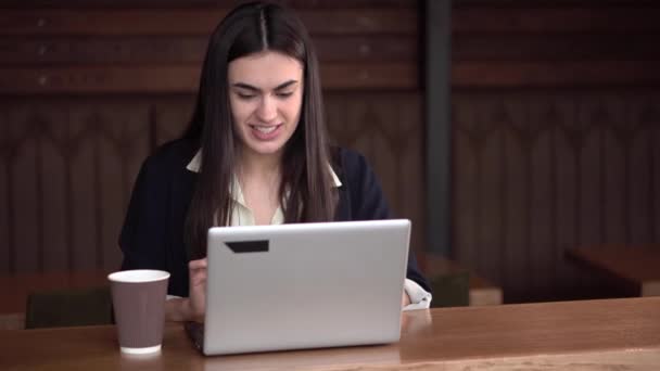 Sorridente ragazza bruna in caffè digitando sul computer portatile e si rallegra con pugni stretti bere caffè — Video Stock