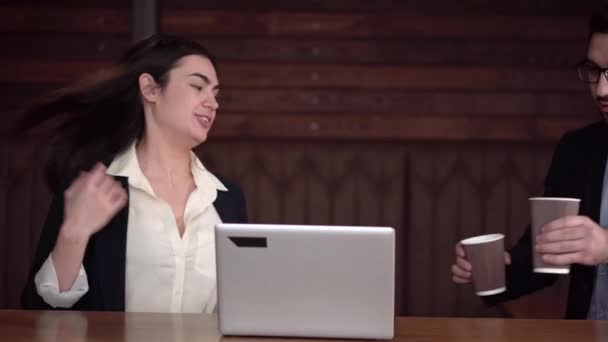 Junge brünette Kerl bringt zwei Kaffee zu einem Mädchen und für sich selbst und sie beginnen, Fall mit einem Laptop zu diskutieren — Stockvideo