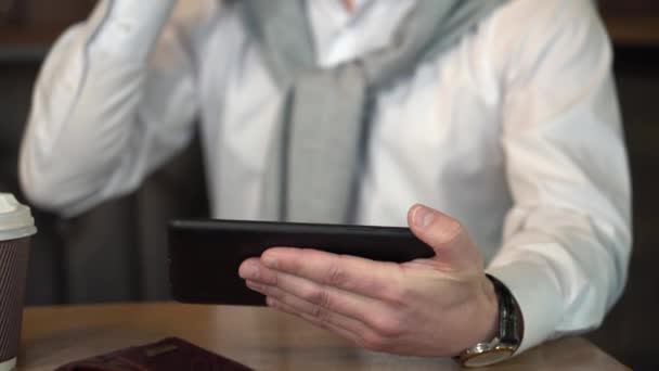 Man volwassen in bril kijkt naar de tablet en spreekt op de telefoon in internetcafé — Stockvideo