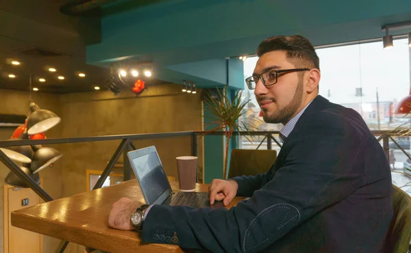 Genç adam gözlük çalışmalar ticaret grafik bir kafede otururken bir laptop
