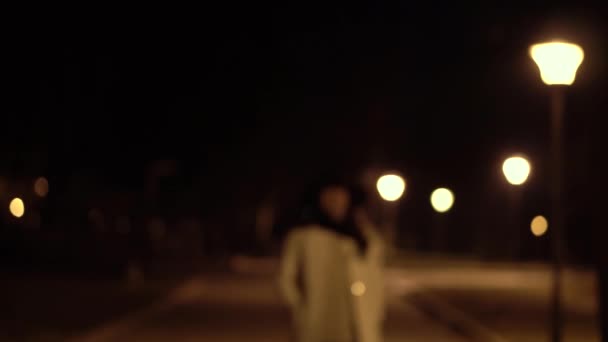 Giovane ragazza bruna in cappello e camice bianco cammina di notte parco inizia a controllare il suo telefono e sorride — Video Stock