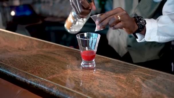 Бармен наливает алкоголь в стакан с клубничным сиропом на стойке, лавовый коктейль — стоковое видео