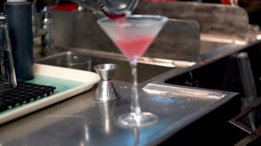 Barmen bardağa bardaktan kokteyl doldurur tezgahın üstünde, Cosmopolitan kokteyli yakın plan