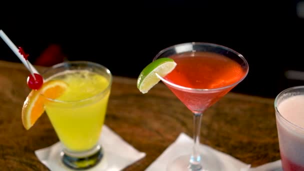 Three glasses with multi-colored alcoholic drinks on bar counter, close-up of cocktails — Stock Video