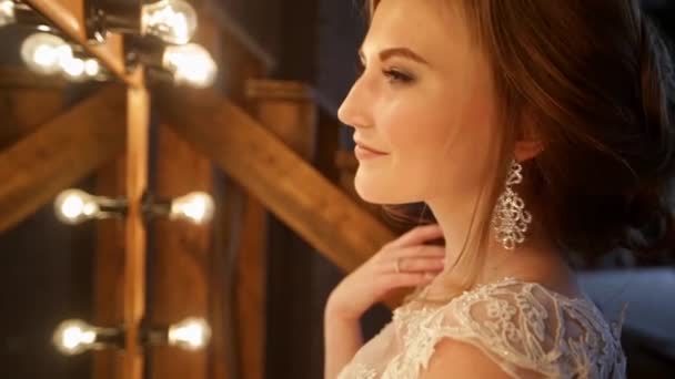 Gros plan de la belle mariée se tient devant un miroir avec des lumières dans un loft intérieur — Video