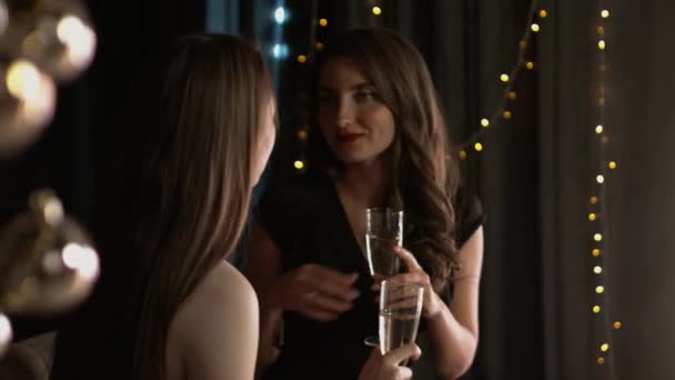 Hermosas chicas con copas de champán emocionalmente hablan en un interior de Navidad — Vídeos de Stock