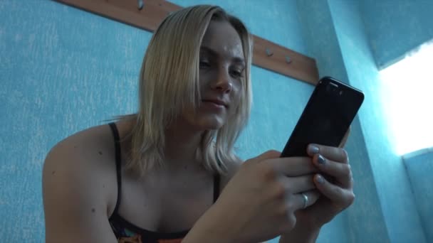 Девушка в купальнике сидит в раздевалке и смотрит на смартфон. Крупный план — стоковое видео
