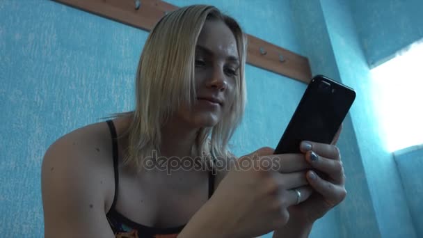 入浴中の少女は、ロッカー ルームで座っているスーツし、スマート フォンに見えます。クローズ アップ — ストック動画