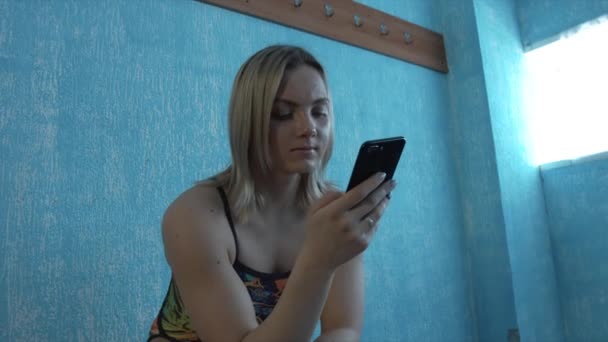 入浴中の少女は、ロッカー ルームで座っているスーツし、スマート フォンに見えます。平均プラン — ストック動画