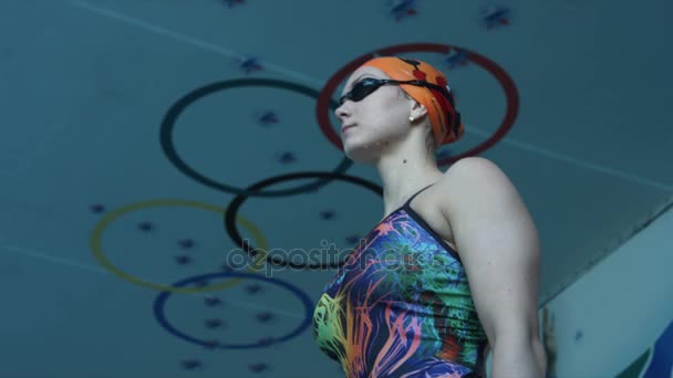 Menina nadadora olha para a piscina antes de saltar no fundo dos anéis olímpicos. Devagar. — Vídeo de Stock