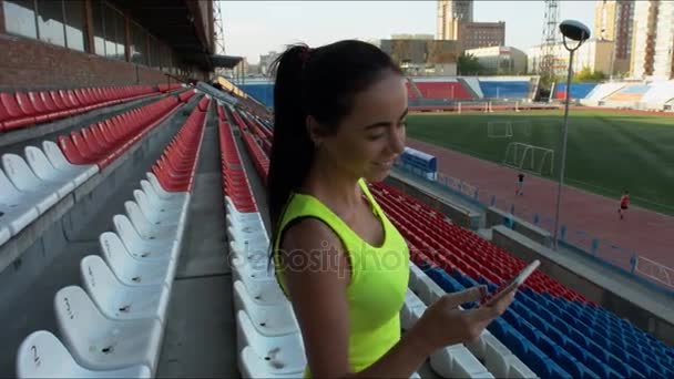 La chica mira el teléfono en un estadio deportivo — Vídeos de Stock