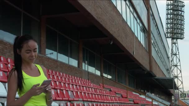 La chica mira el teléfono en un estadio deportivo — Vídeos de Stock