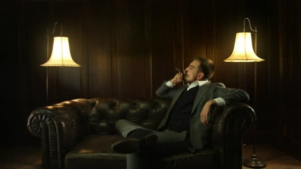 Schöner junger Mann im teuren Anzug, der in der Bar eine Zigarre raucht — Stockvideo