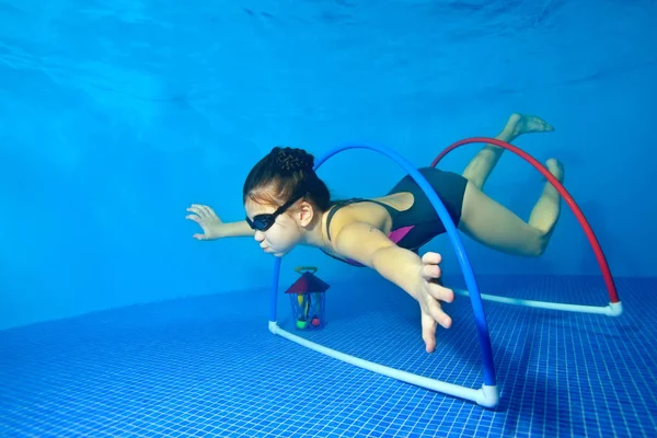 Meisje zwemt speelt sport onder water in het zwembad op een blauwe achtergrond en zweeft door de hoepels onderaan. Fotograferen onder water. Portret. Horizontale oriëntatie — Stockfoto
