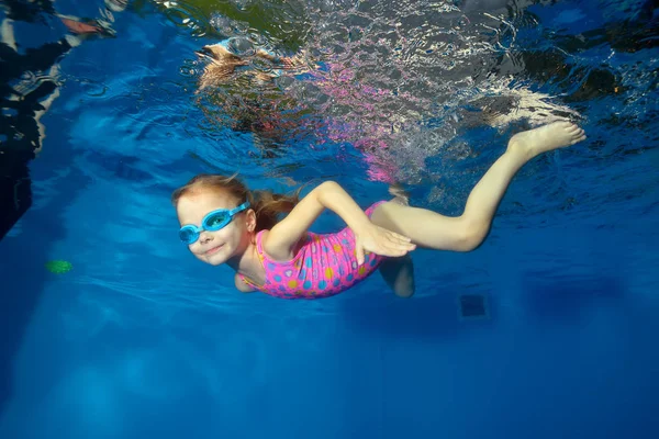 Boldog kis baba víz alatti úszik a medencében, néz a kamerába, és mosolyog. Portré. Víz alatti fotózáshoz. Fekvő tájolású — Stock Fotó