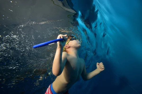 Un niño flota bajo el agua desde el fondo de la piscina hasta la superficie . — Foto de Stock