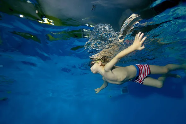 小さな少年泳ぐ水中両腕とプールで青い背景上のスポーツします 肖像画 水の下からの眺め 横向き — ストック写真