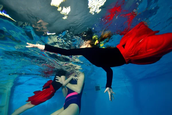 Familia, madre y dos hijas nadan y juegan bajo el agua en la piscina sobre un fondo azul —  Fotos de Stock