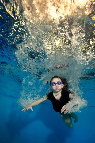 Glückliches kleines Mädchen schwimmt und spielt unter Wasser in den Blasen auf blauem Hintergrund — Stockfoto