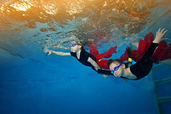 Underwater two little girls are swimming and playing. Dive to the bottom on a blue background in the light.