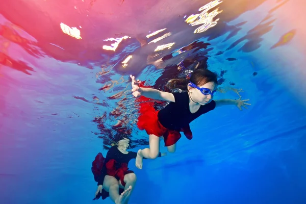 Dos niñas nadan bajo el agua sobre un fondo de luces rojas . — Foto de Stock