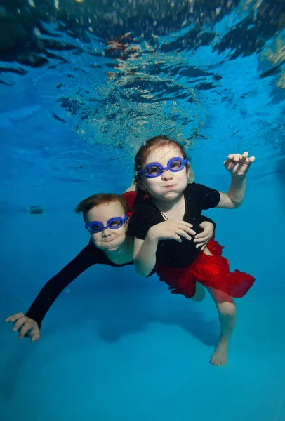 Dos niñas nadando y posando bajo el agua y mirándome sobre el fondo azul . — Foto de Stock