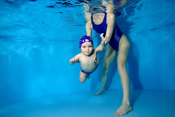Mamá ayuda a su hijo a nadar bajo el agua en la piscina sobre un fondo azul . — Foto de Stock