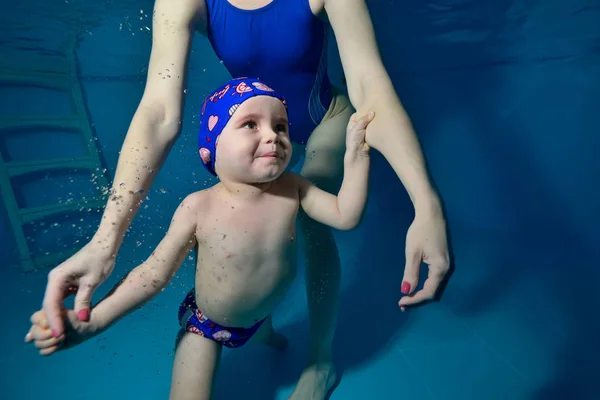 Niño nada bajo el agua en la piscina, se aferra a su madre, y la madre lo asegura . — Foto de Stock