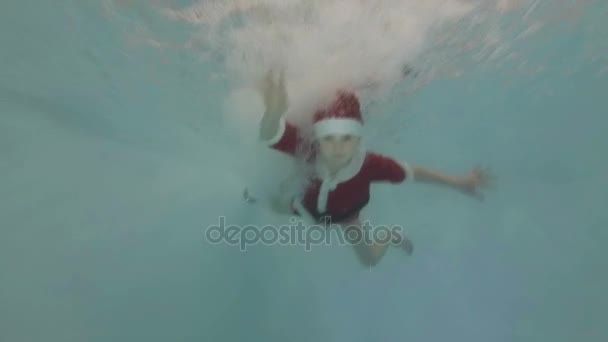 Niño feliz en traje rojo Santa Claus posa bajo el agua en la piscina — Vídeo de stock