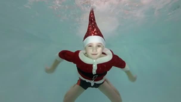 Anak kecil yang bahagia dengan pakaian merah Santa Claus berenang di bawah air di kolam renang — Stok Video