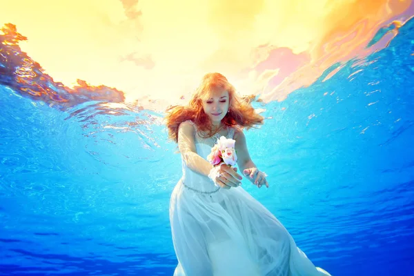 İnanılmaz güzellik Kızıl saçlı kız sualtı günbatımında bir gelinlik içinde yüzüyor. Portre. Yatay görünüm. Su altından çekim