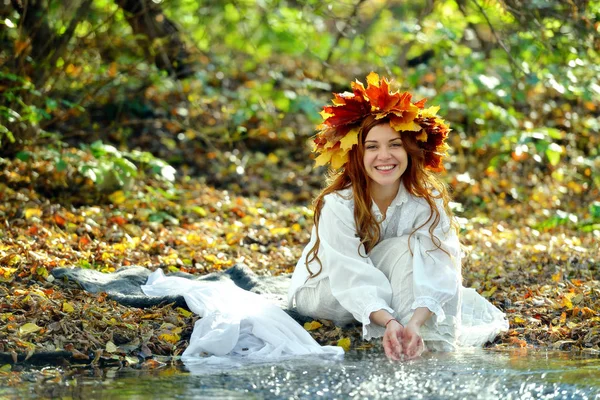 白いドレスを着て 黄色の葉からの花輪で笑っている女の子が座っていると 秋の日 サニーの水のスプレーで遊んで — ストック写真