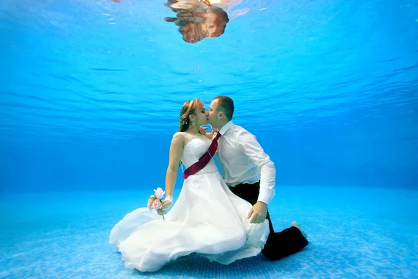 Les mariés en robes de mariée embrassent et embrassent sous l'eau au fond d'une piscine. Portrait. Orientation paysage. Tir sous l'eau — Photo