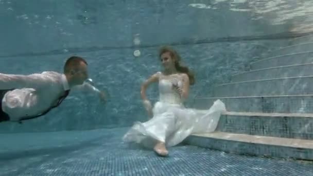 El novio nada bajo el agua a la novia que se sienta en el fondo de la piscina y besa su mano — Vídeo de stock