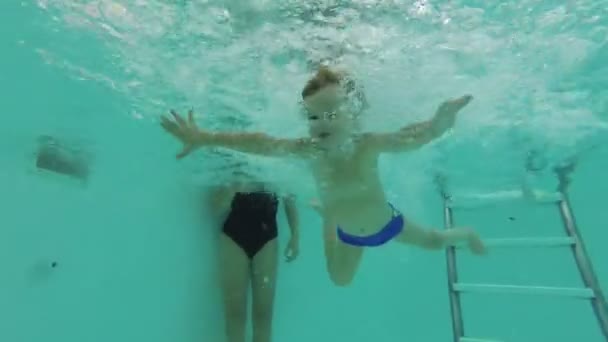 Un niño se sumerge en la piscina, nada bajo el agua con los ojos abiertos y mirando a la cámara — Vídeo de stock