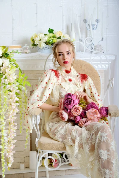 Belle fille assise et posant sur un tabouret vintage dans le Studio avec un bouquet de fleurs dans ses mains et me regarde . — Photo